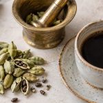 Păstăi verzi de cardamom, mojar de alamă și o ceașcă de cafea