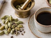 Păstăi verzi de cardamom, mojar de alamă și o ceașcă de cafea