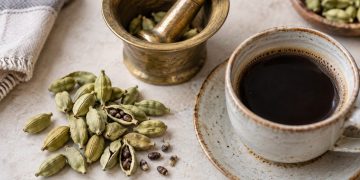 Păstăi verzi de cardamom, mojar de alamă și o ceașcă de cafea