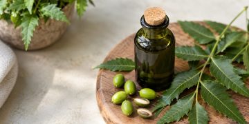 Sticlă cu ulei de neem, frunze și semințe de neem pe o tăviță de lemn