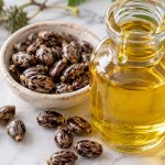 Sticlă cu ulei de ricin gălbui și semințe de ricin pe marmură