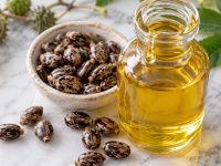 Sticlă cu ulei de ricin gălbui și semințe de ricin pe marmură