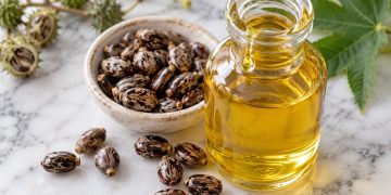 Sticlă cu ulei de ricin gălbui și semințe de ricin pe marmură